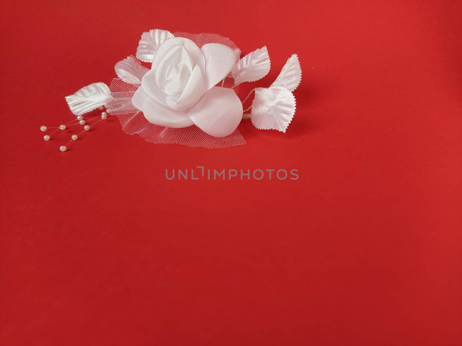 A stunning white rose stands out beautifully against a rich red background, complemented by soft leaves and small pearl accents, ideal for a wedding setting.