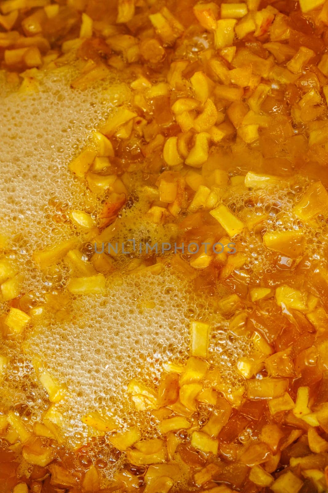 full-frame background and texture of sliced yellow apples boiling in syrup during confiture cooking.