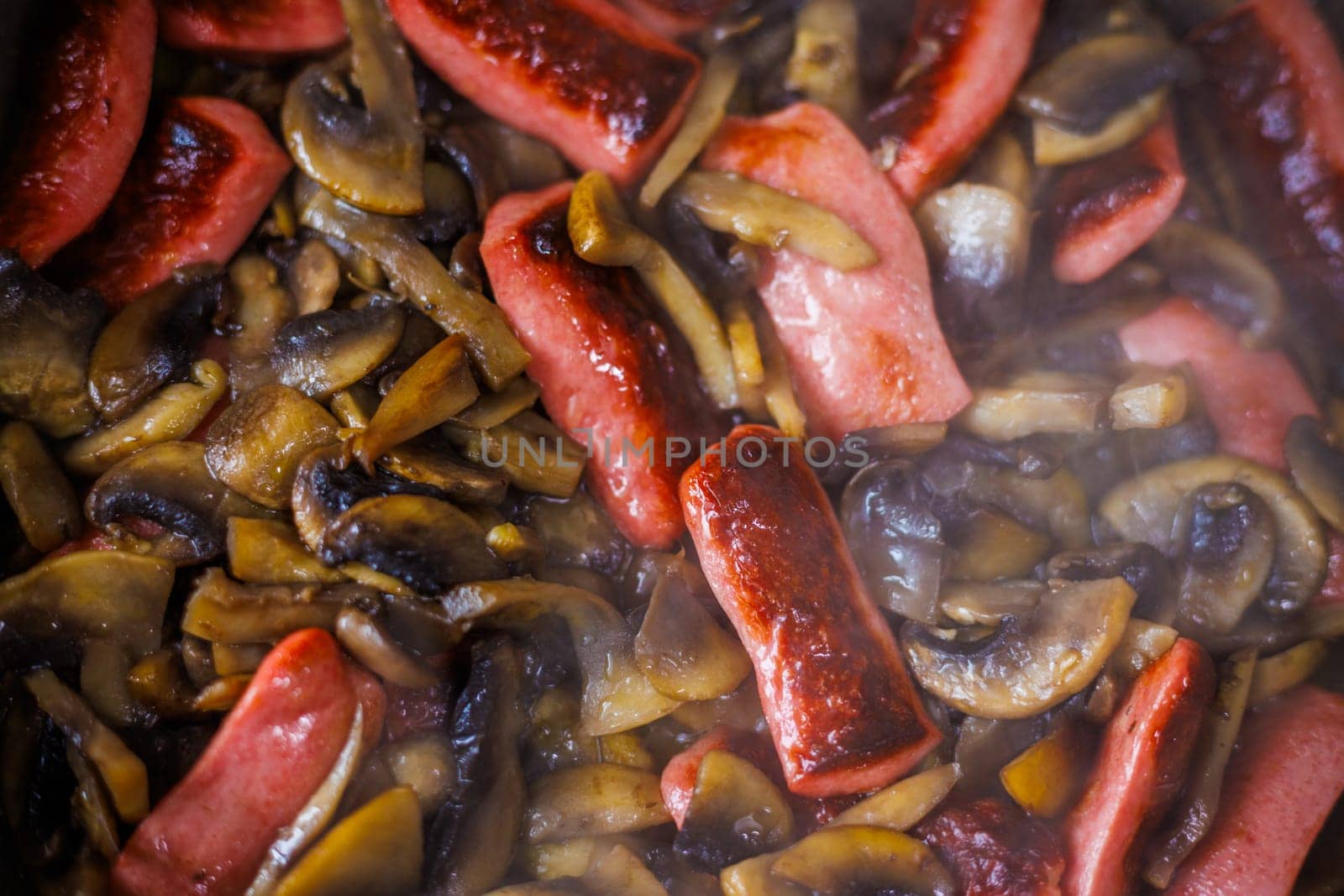 closeup view of roasting cut champignon mushrooms and sausages.