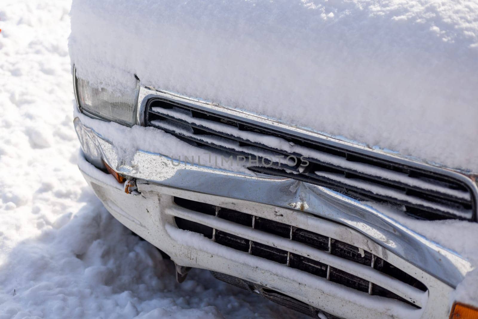 snow covered white SUV car with damaged front bumper at sunny winter day