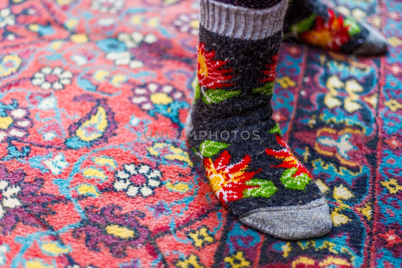 legs in warm woven wool socks standing on red ornate carpet floor at home backlit with a window light