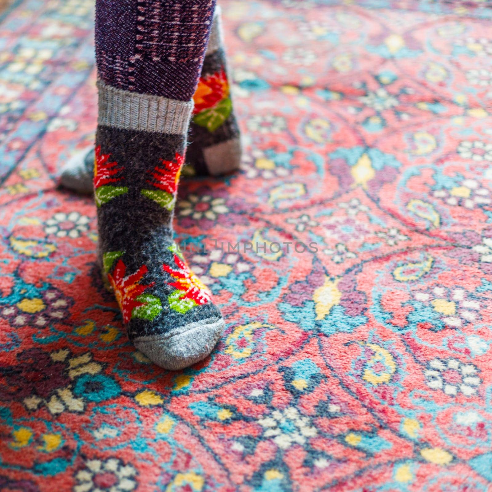 legs in warm woven wool socks standing on red ornate carpet floor at home backlit with a window light