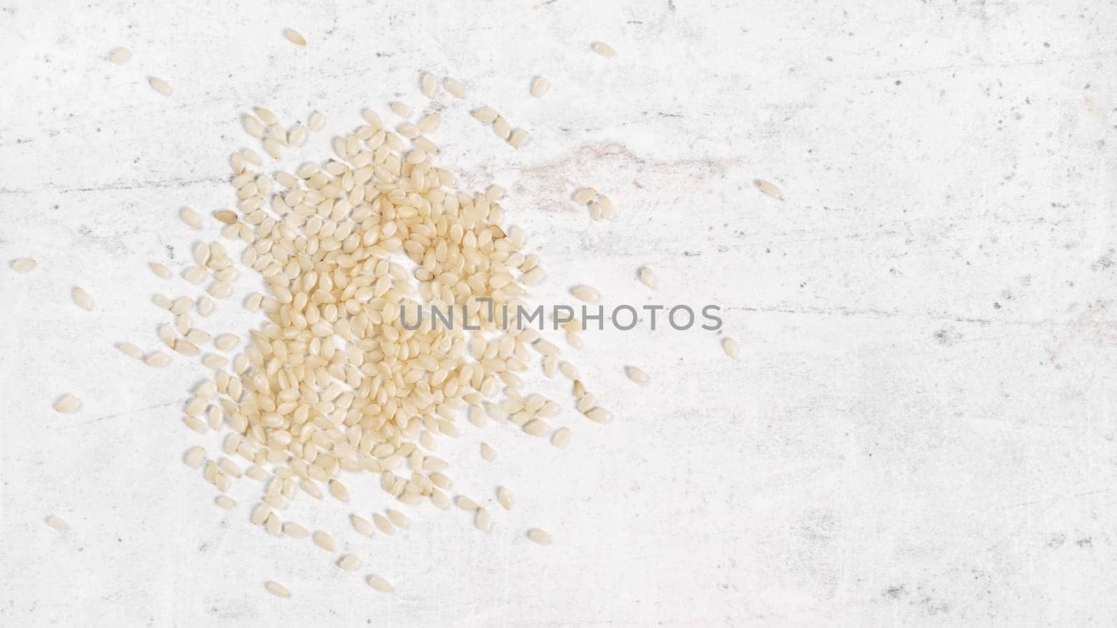 White sesame - Sesamum indicum - seeds on white stone like board, view from above, space for text right side