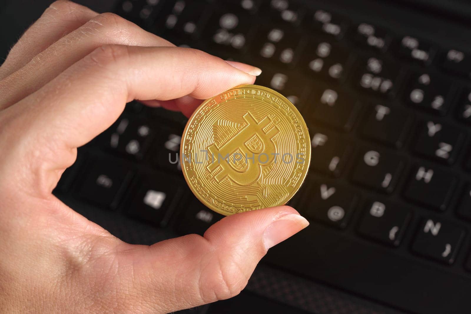 Woman hand holding golden coloured bitcoin coin over black laptop keyboard