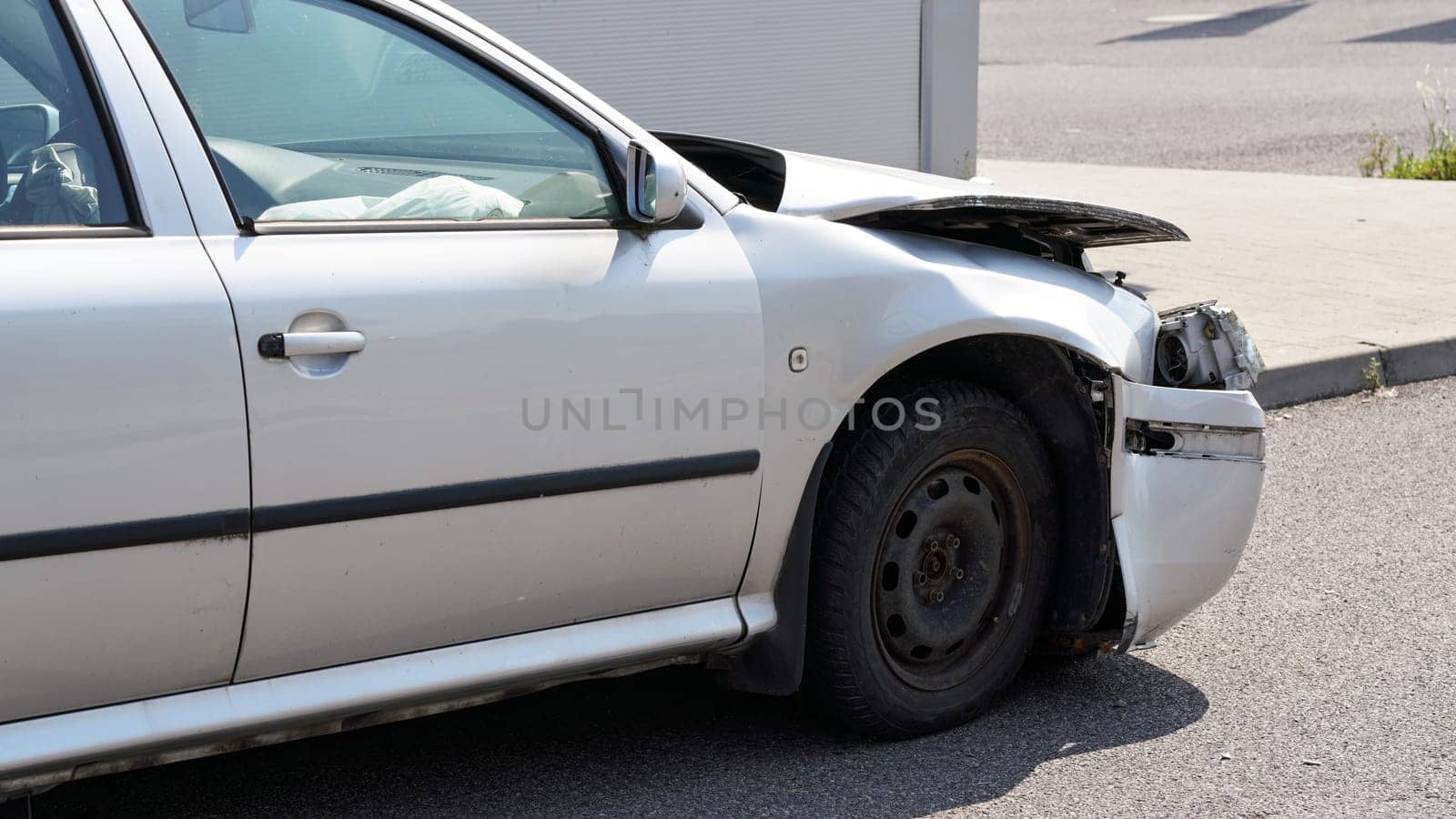 Crashed car standing on road next to curb, side view with demolished front and used airbag inside visible