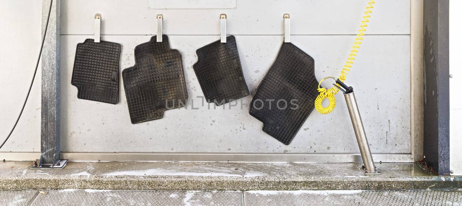 Black rubber car mats hanging on steel pegs to dry in carwash after being washed