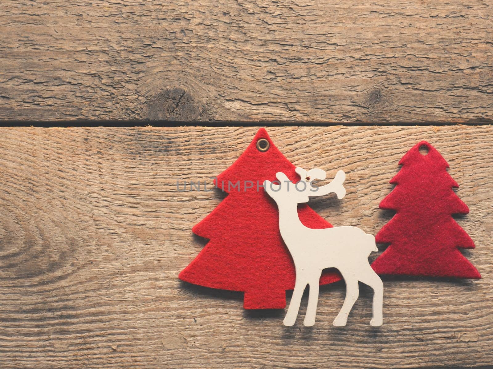 Christmas background with a wooden deer and red tree shapes on a rustic wooden plank