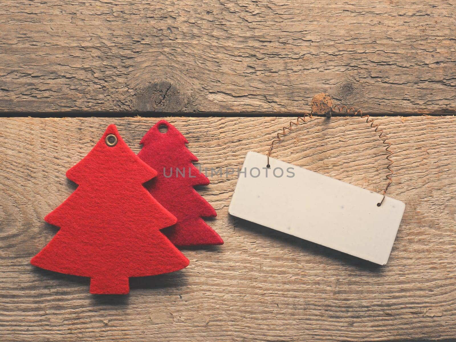 Christmas background with a wooden blank sign and red tree shapes on a rustic wooden plank