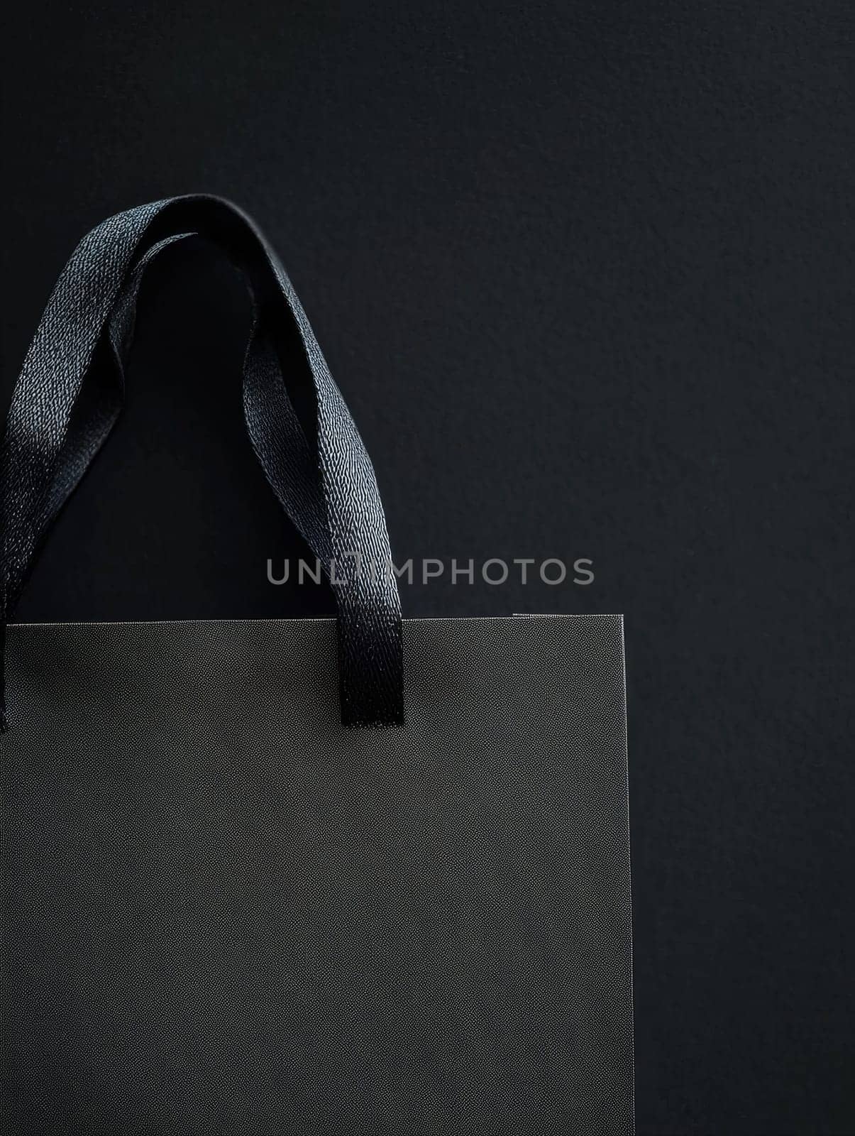 A sleek black shopping bag with textured handles, set against a dark background, providing ample copy space.