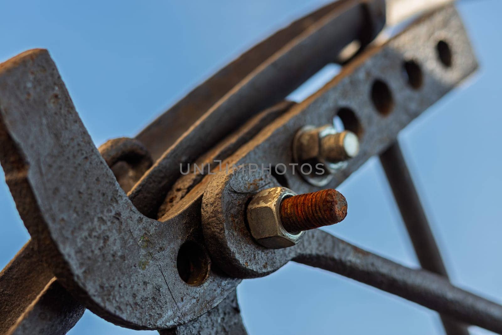 Rusty metal clamp holding construction elements together with visible threaded connection and a blue sky in the background