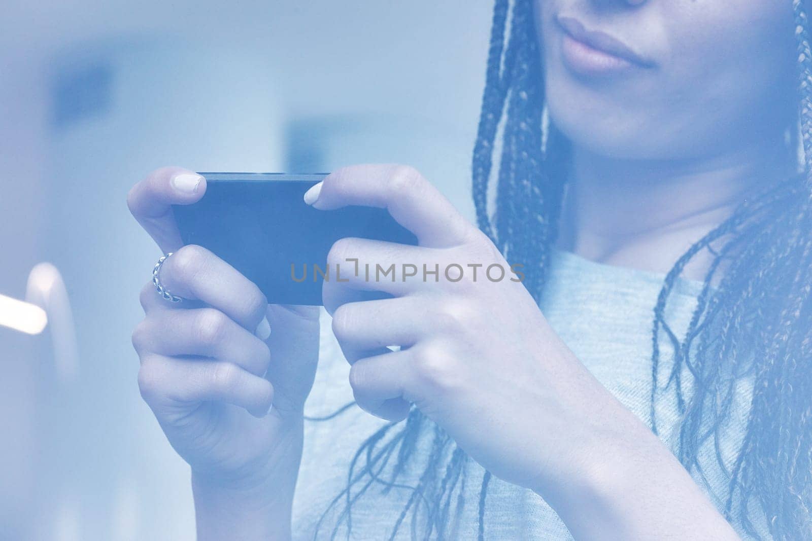 Young woman using her smartphone at home, scrolling through social media and checking messages, with natural light highlighting her hands and stylish jewelry