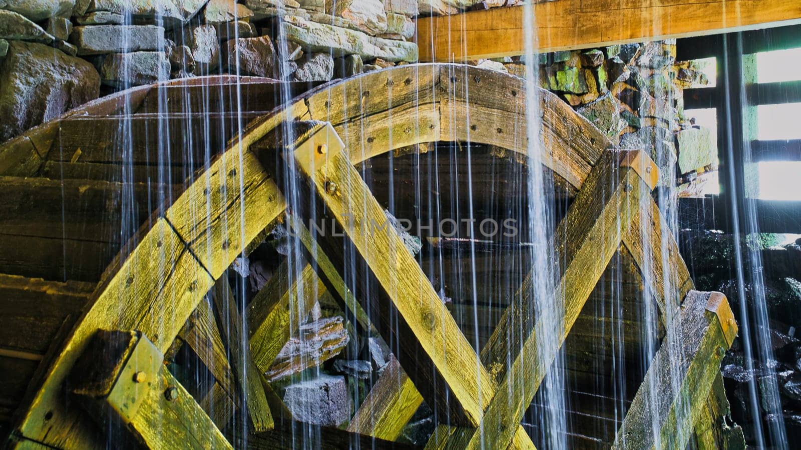 Old wooden waterwheel splashed by falling water. Picture from a watermill in Sweden by a stream.