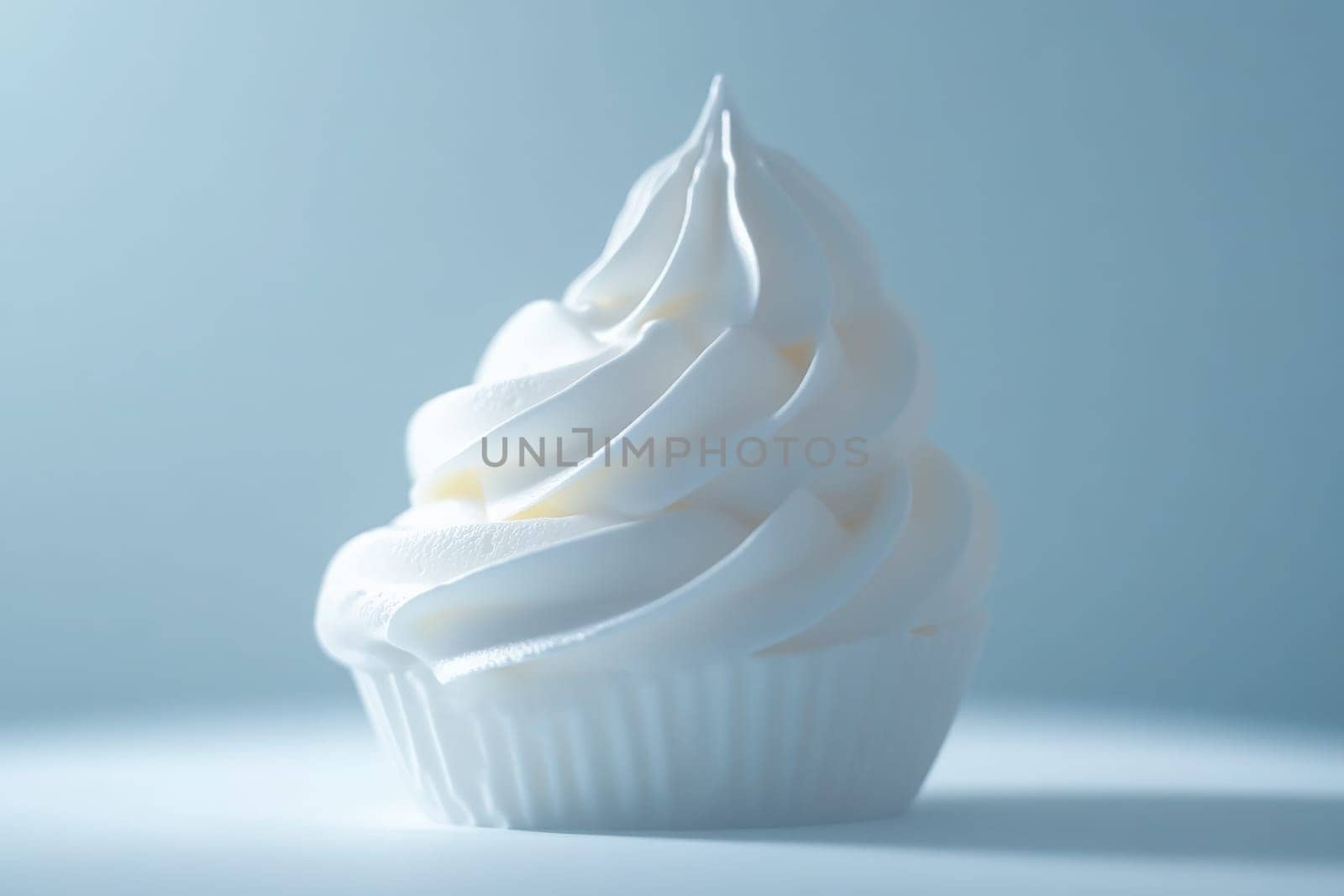 A perfectly crafted whipped cream swirl sits elegantly on a cupcake, showcasing its smooth texture and pristine white color. The soft blue background enhances its minimalist appeal.
