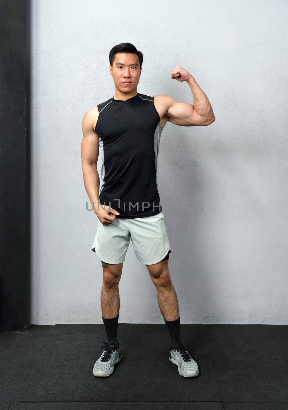 Empowered and strong, a fitness enthusiast male flexes his biceps under the stark, vibrant light of a bustling gym, revealing the result of his perseverance and dedication.