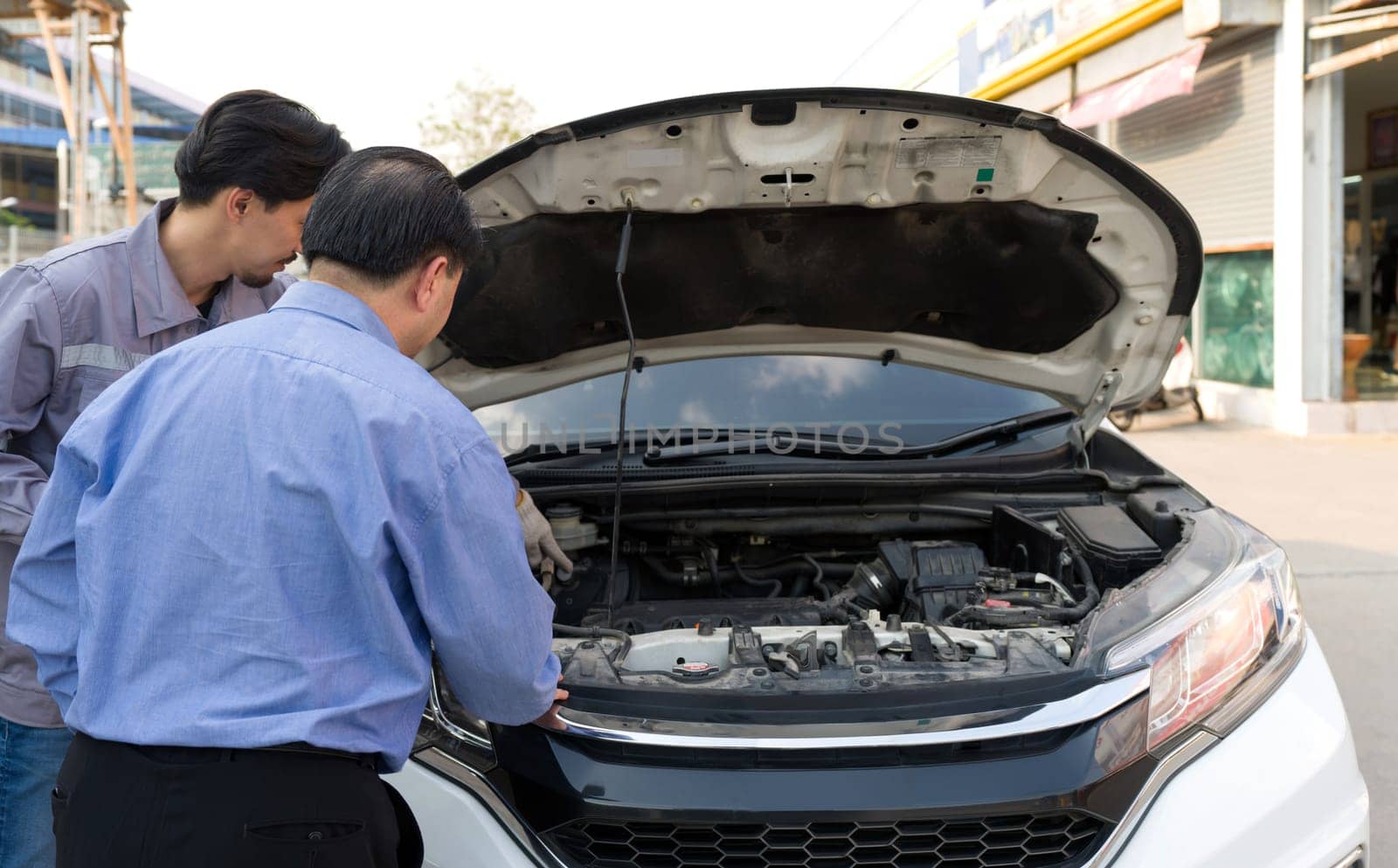Two guys are standing by a car with the hood open, staring at the engine inside. Back view