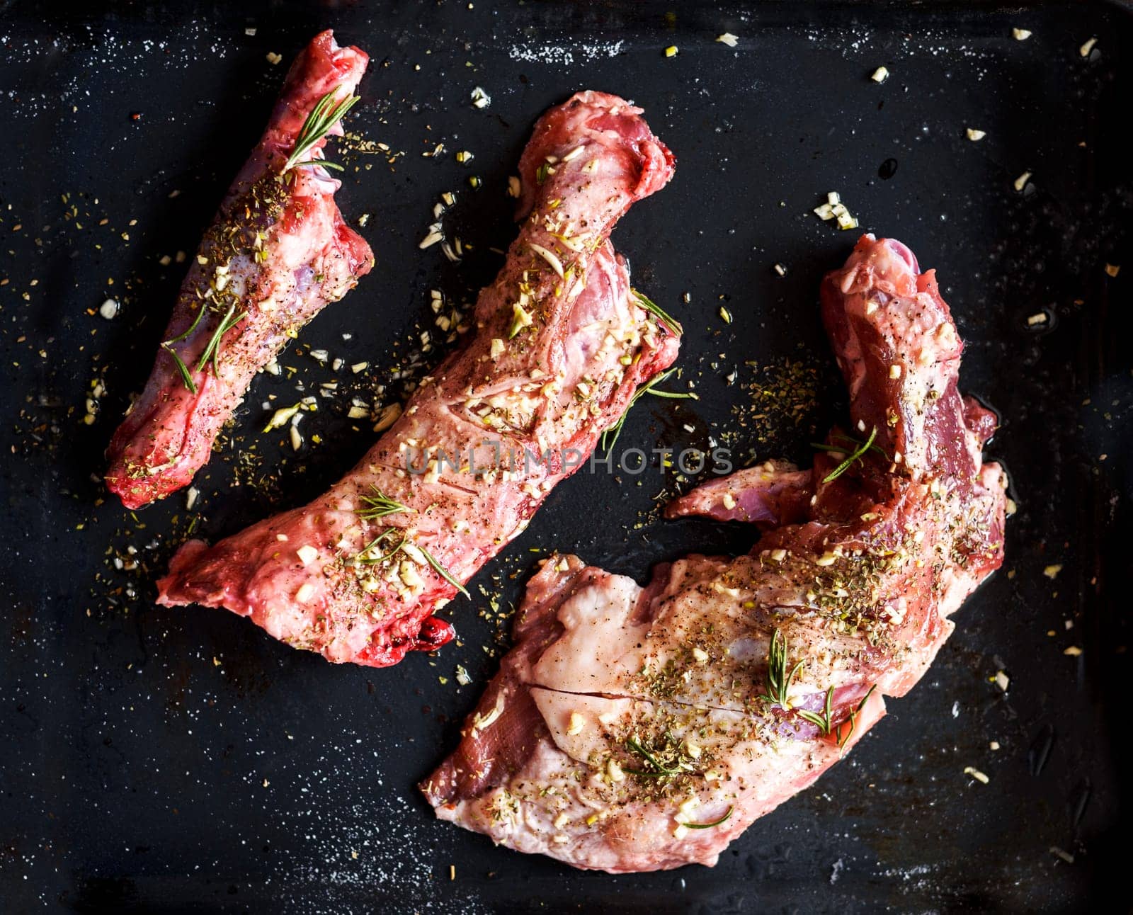 Lamb meat bbq preparation. Lamb chops with spices and rosemary on black rustic plate from above. Top view of restaurant cuisine barbecue.