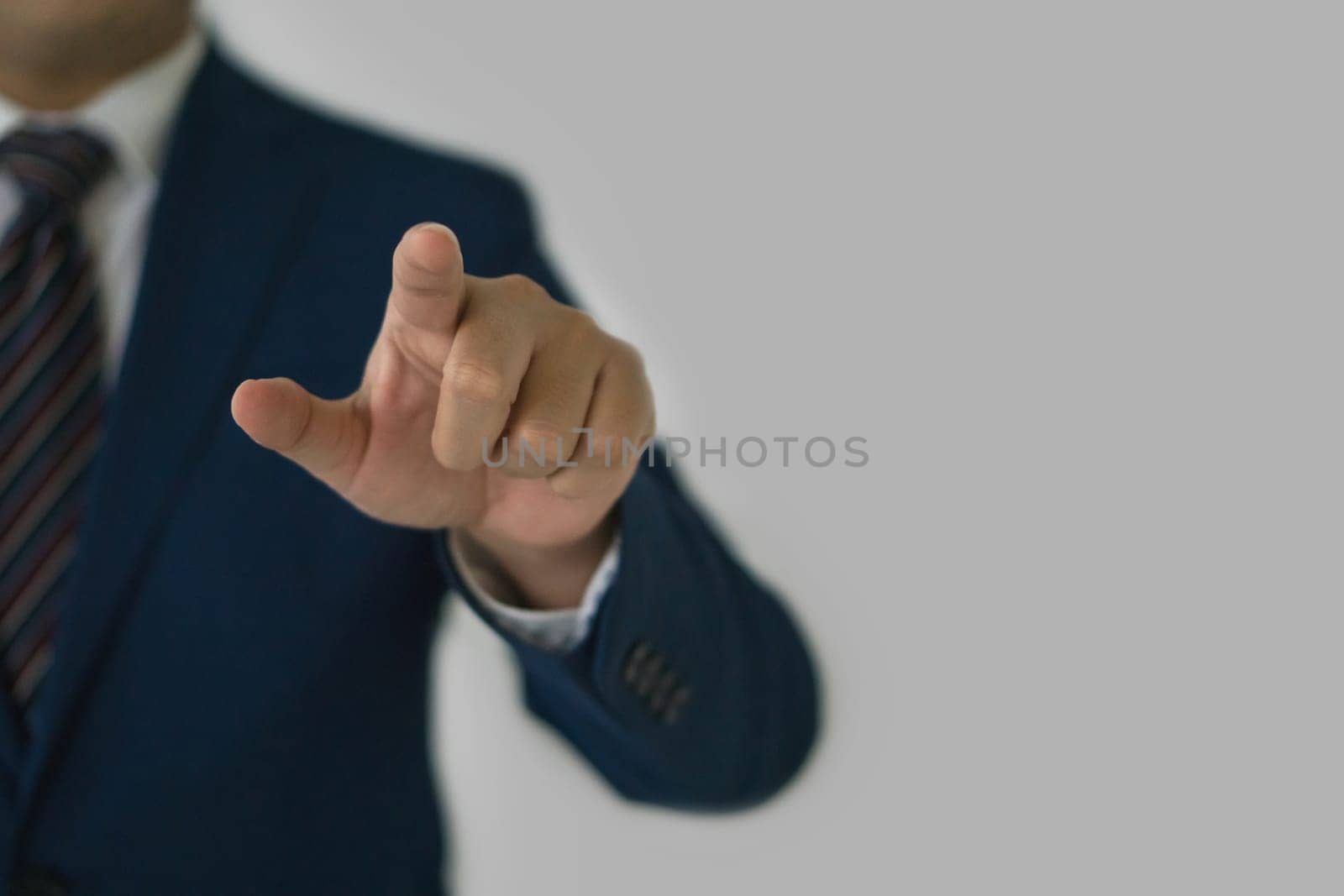 A businessman in smart blue suit and tie pointing finger toward with his hand. Portrait on gray background, studio shot.