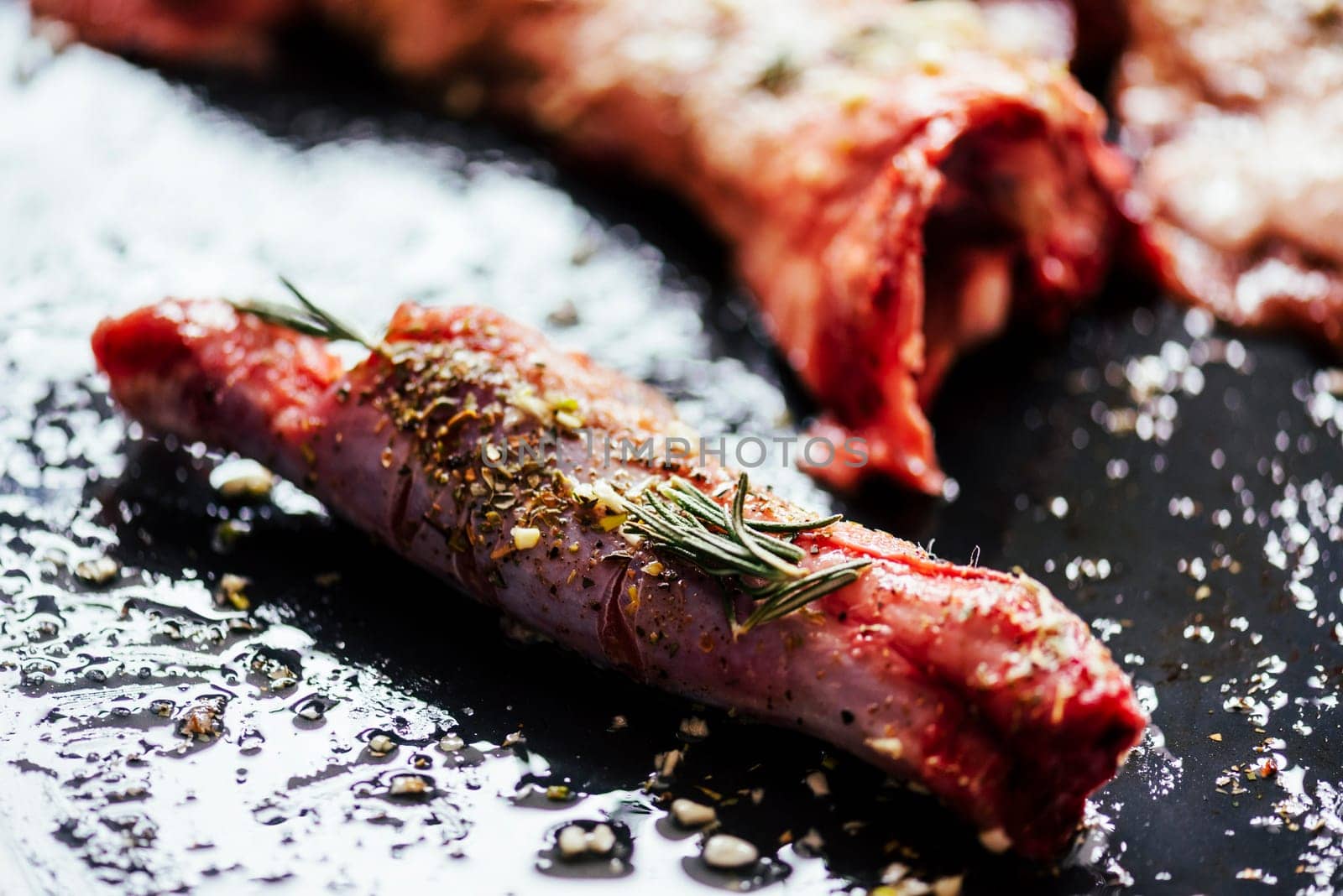 Lamb meat bbq preparation. Closeup of lamb chops with spices and rosemary on black rustic plate. Restaurant cuisine barbecue dish.