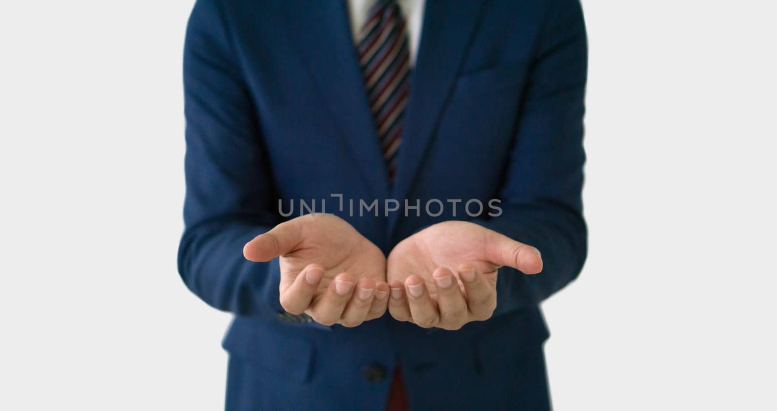 A businessman in smart blue suit and tie standing with his hand open and facing up, suggesting a gesture of offering, explaining, or questioning. Portrait on white background, studio shot.
