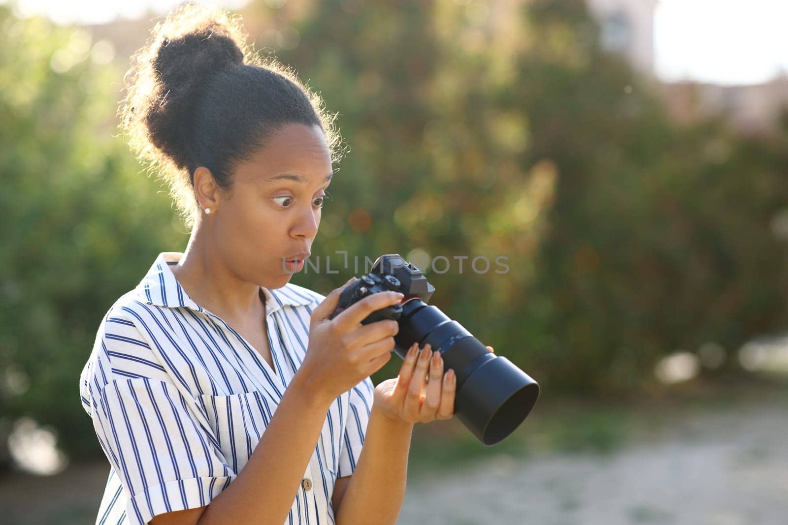 Surprised black photograper checking result on mirrorless camera in a park