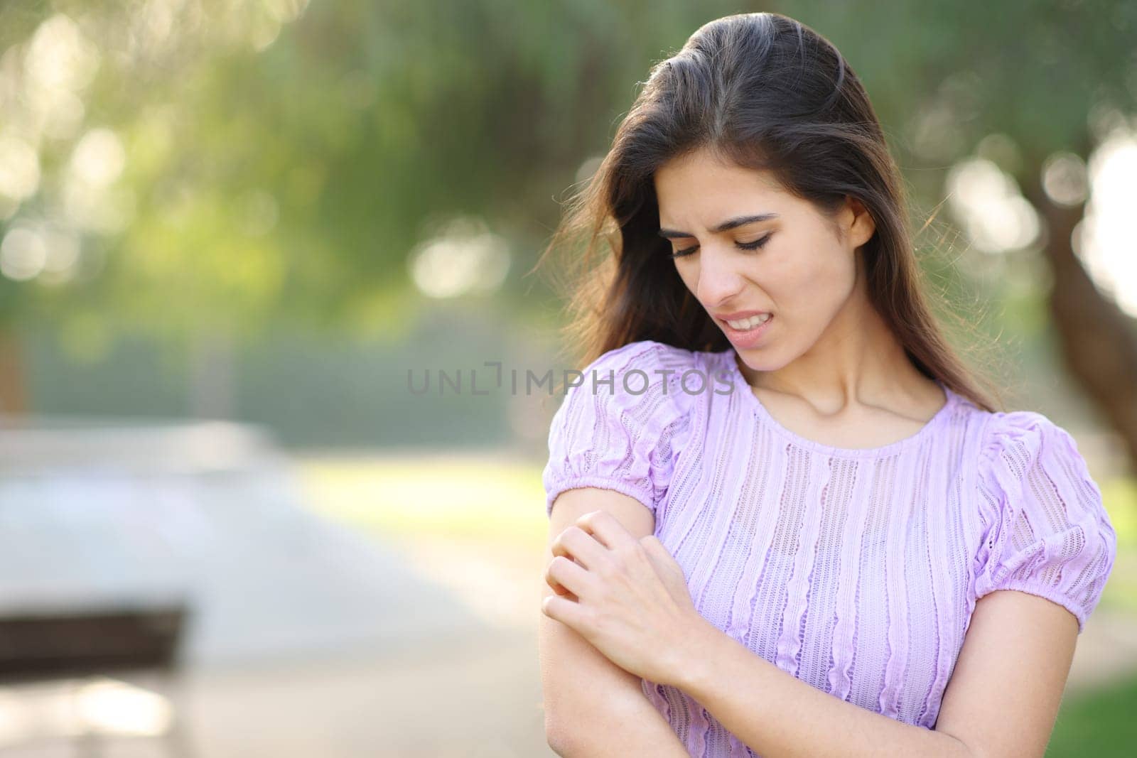 Woman scratching arm standing in a park in summer season