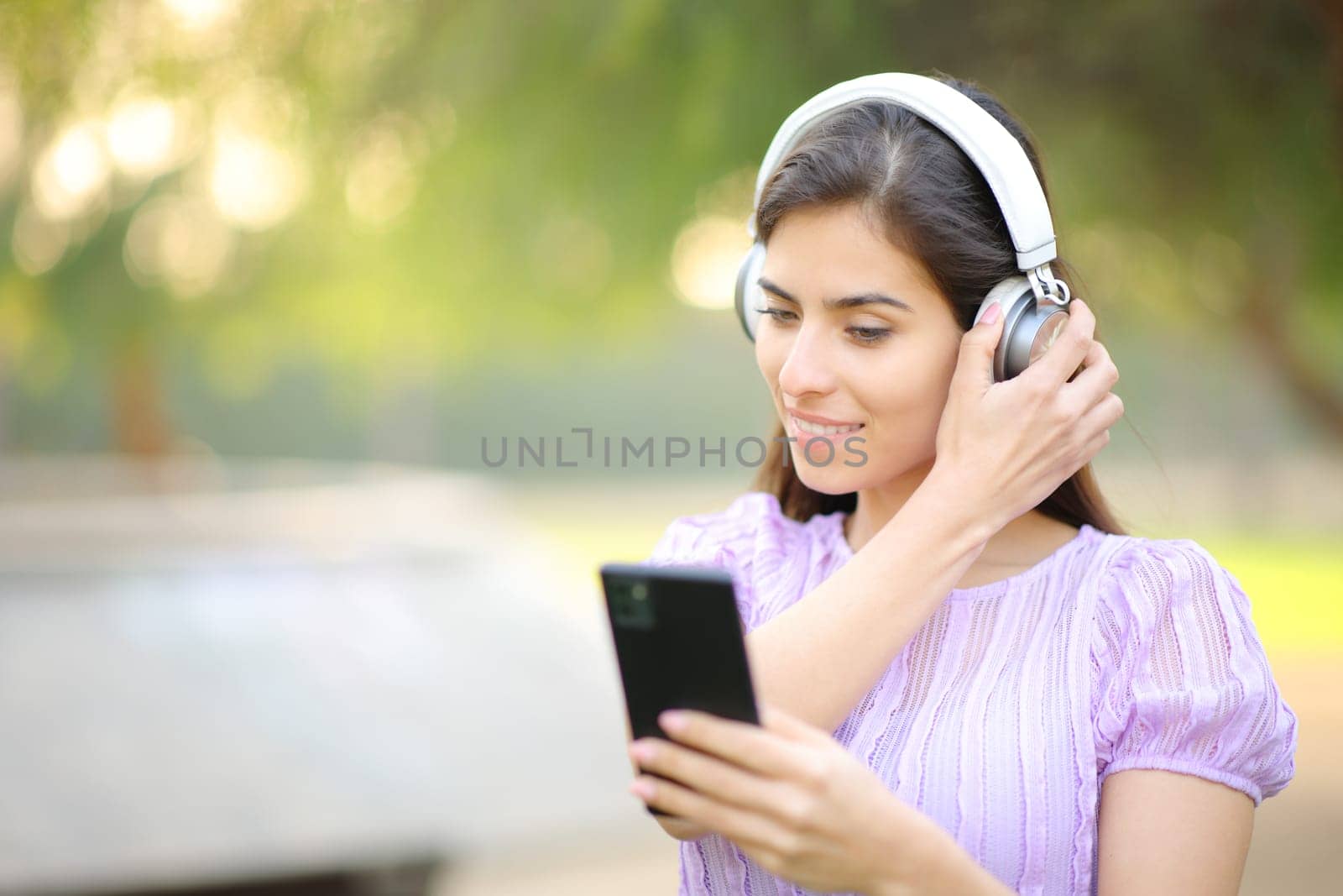 Woman putting headphone watching phone content in a park