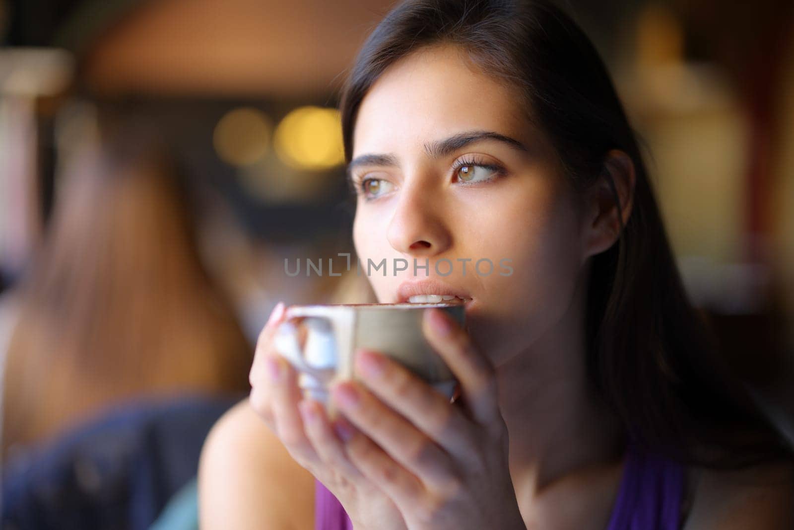Pensive woman drinking coffee looking away in a restaurant