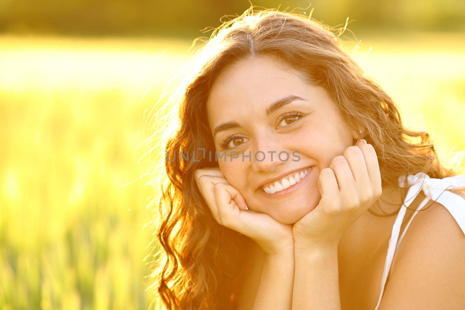 Happy woman smiling with perfect teeth posing in a field at sunset