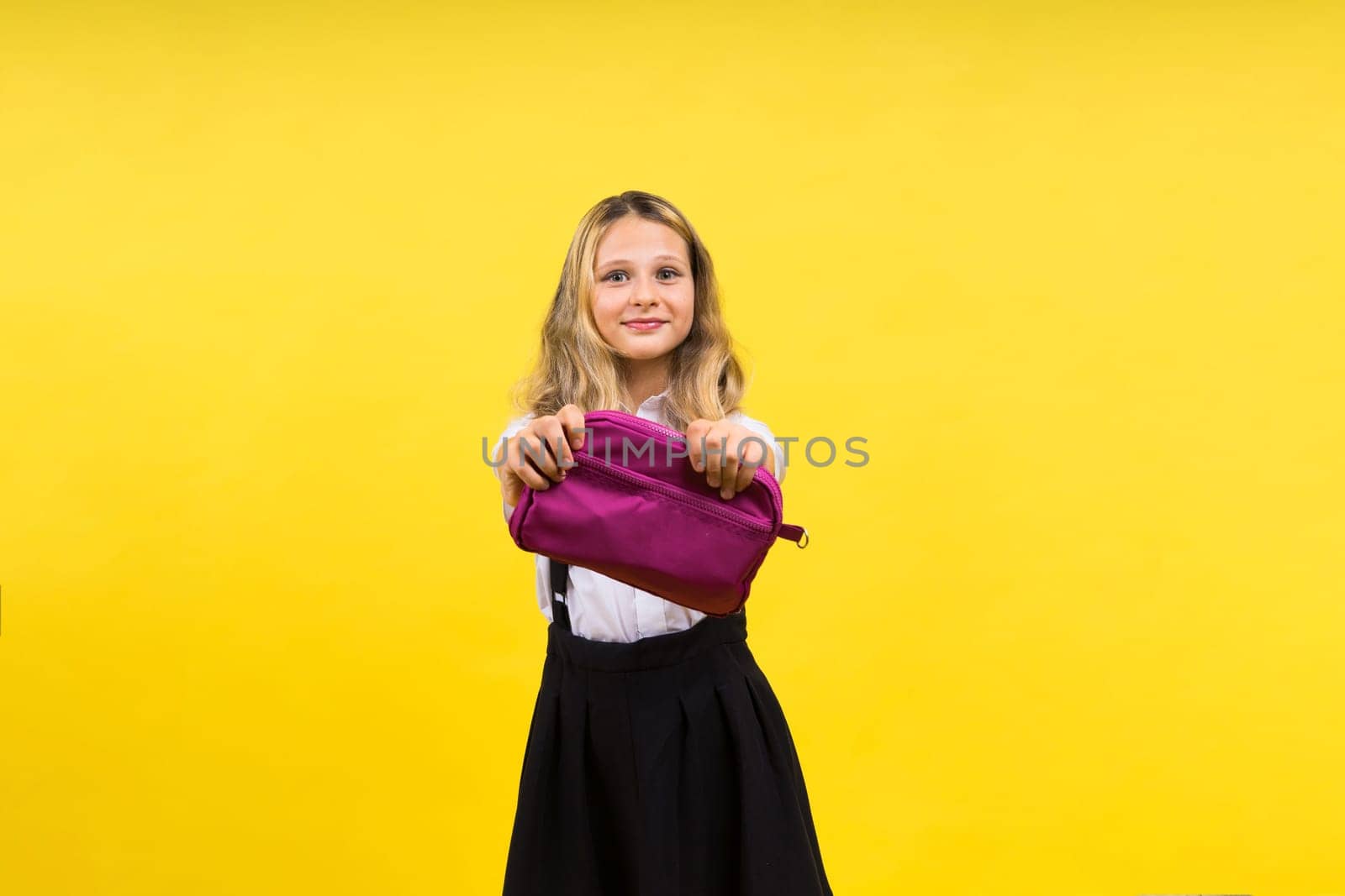 Little teenager girl with pencil case on a yellow background