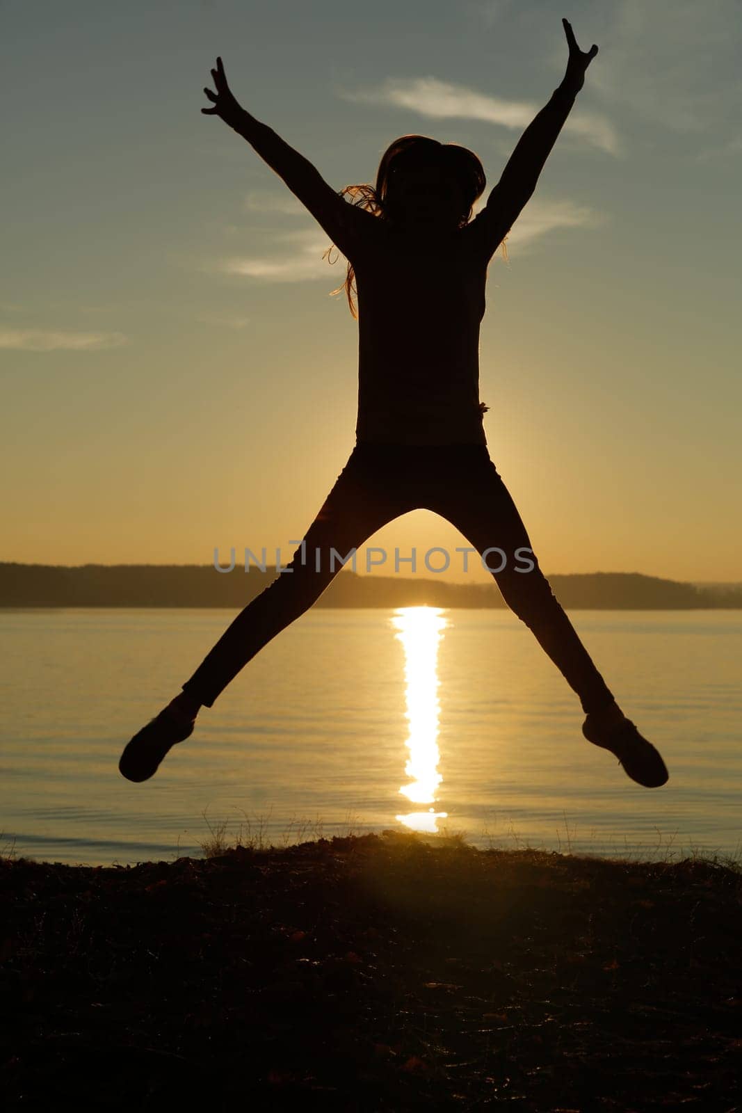 A joyful and energetic silhouette leaps gracefully against a stunning sunset over calm and serene waters
