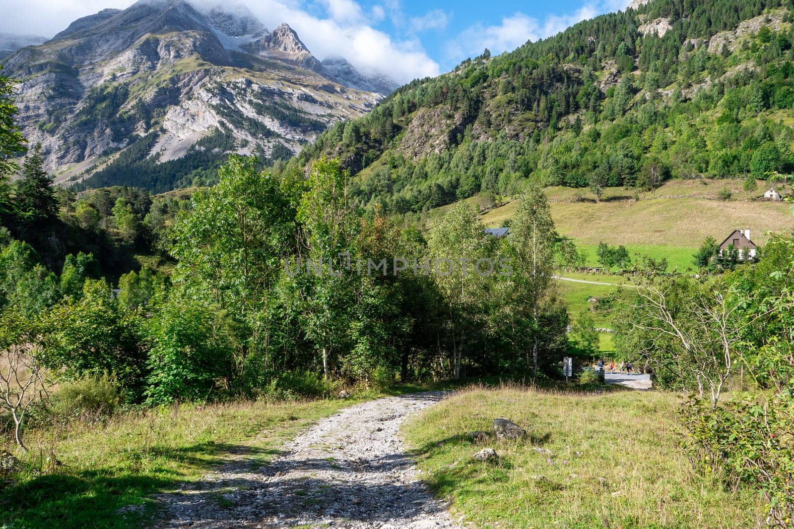 A mountain range with a path leading to a house. The path is rocky and the grass is green