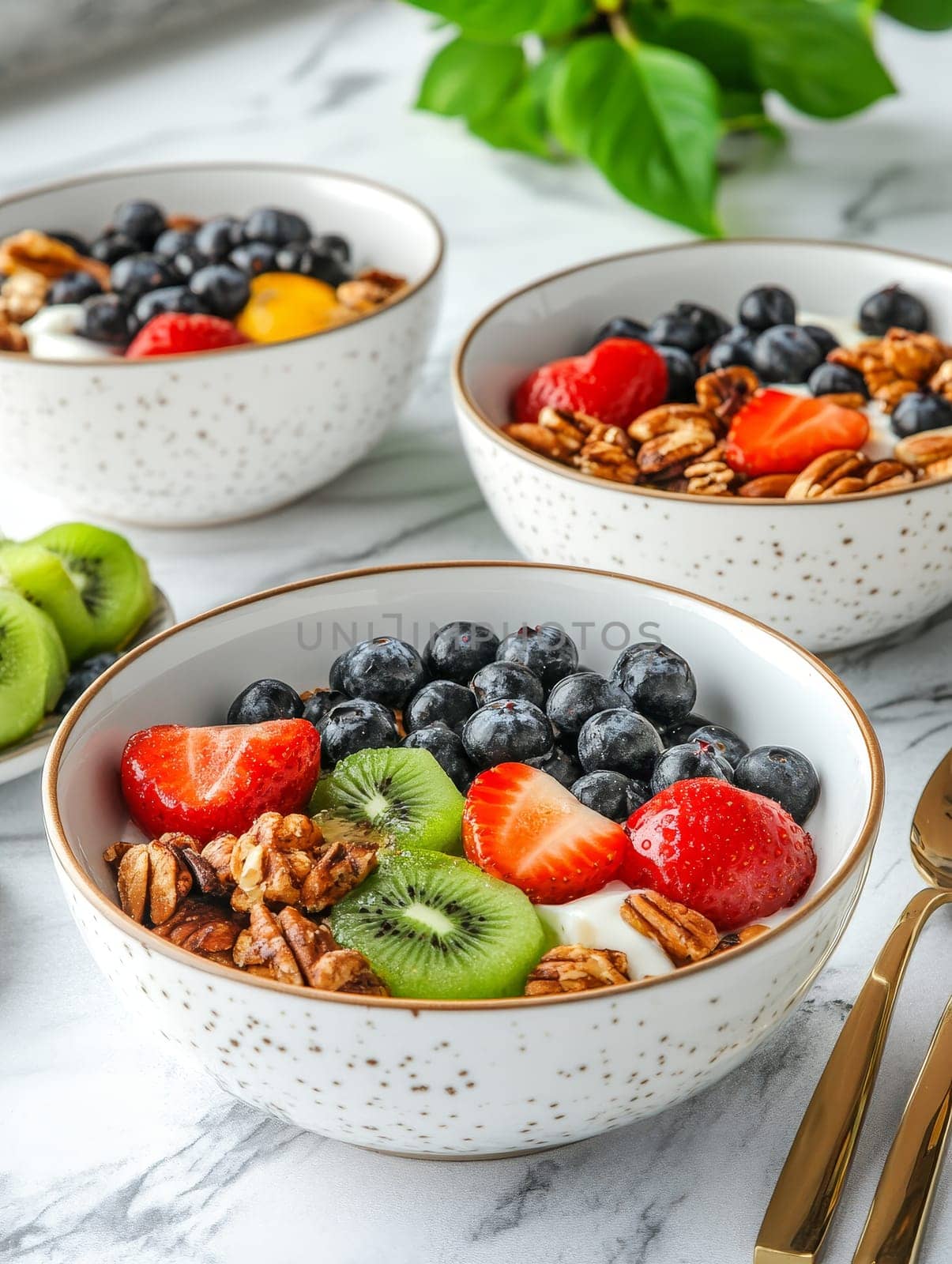 Three white speckled bowls filled with a variety of fresh fruits, berries, and nuts, showcasing a colorful and nutritious breakfast spread on a marble countertop.