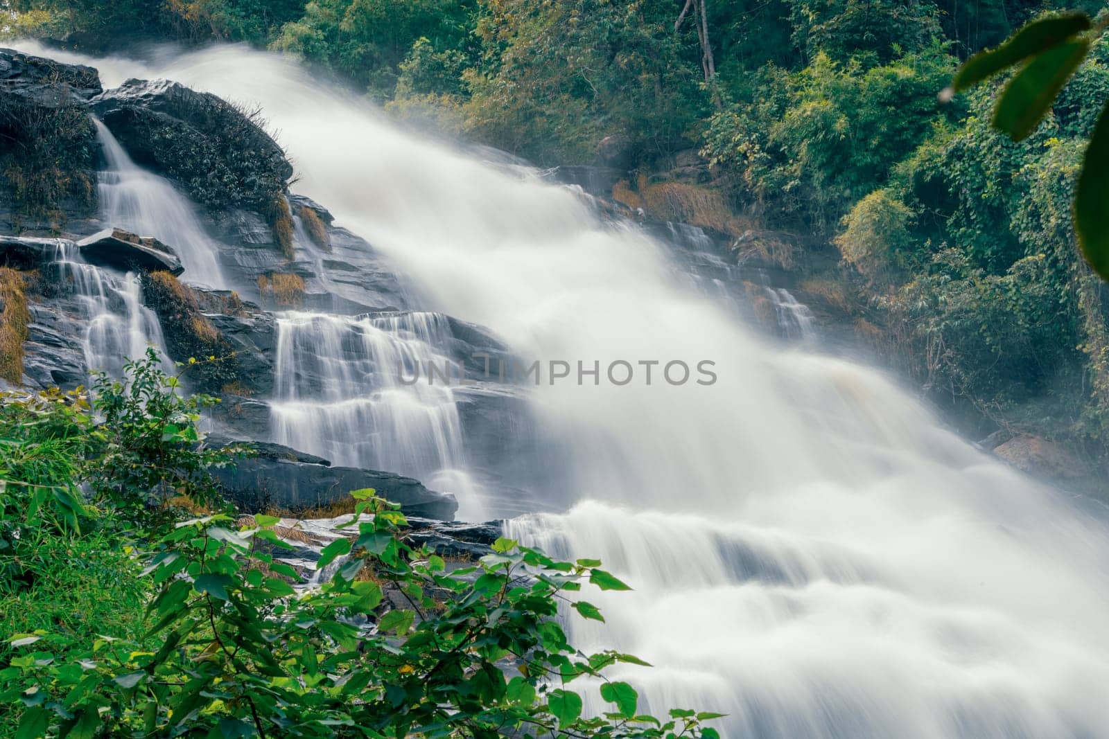 Beautiful waterfall with a lush green forest in the background. The water is flowing down the rocks and creating a beautiful scene. Sustainable waterfall in lush forest promoting water sustainability.
