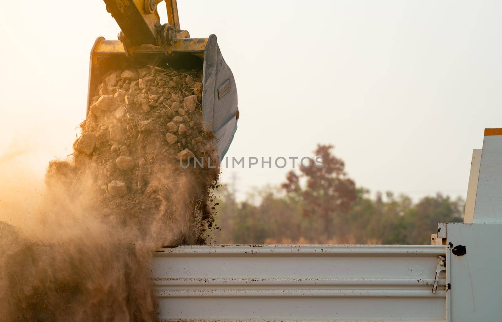 Backhoe loading soil into heavy duty dump truck at construction site. Crawler excavator transporting dirt with powerful bucket. Heavy construction machinery. Industrial earthmoving equipment in action