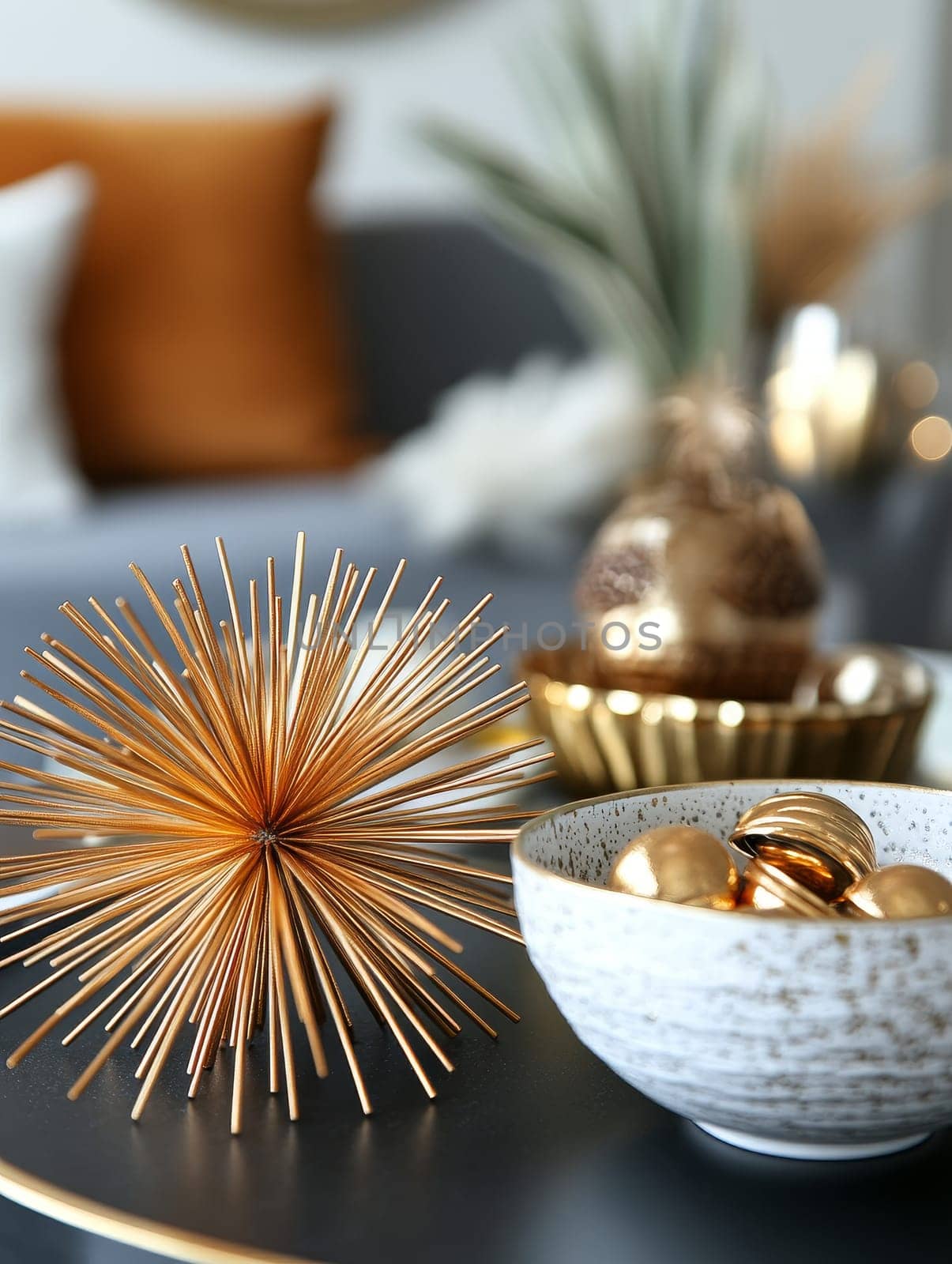 Elegant gold home decor items including a spiky starburst sculpture and metallic ornaments in a ceramic bowl, set against a blurred background.