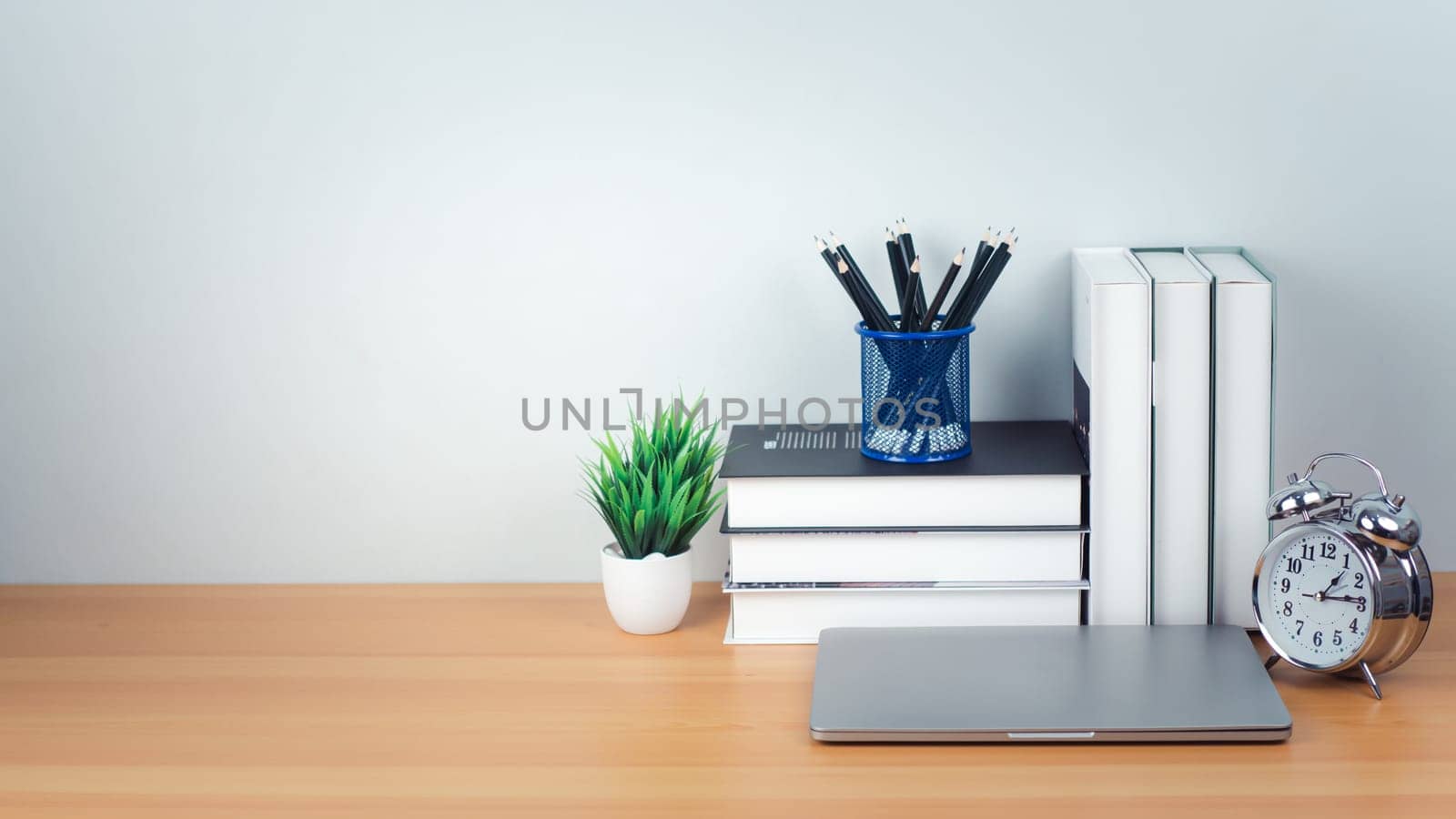 Workspace mock up white table top with laptop, Pencils, Book, Alarm clock and green houseplant. Copy space desk with copy space for products display montage. Minimalist white workplace with supplies.