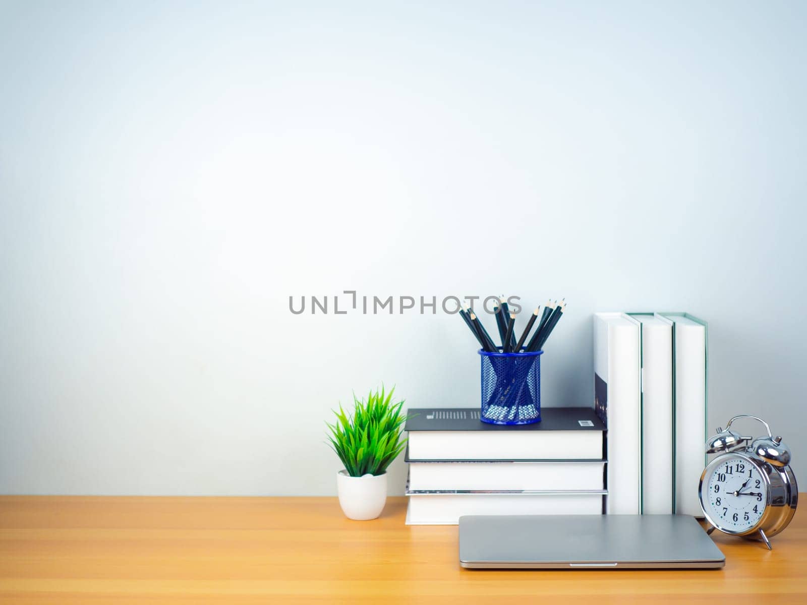 Workspace mock up white table top with laptop, Pencils, Book, Alarm clock and green houseplant. Copy space desk with copy space for products display montage. Minimalist white workplace with supplies.