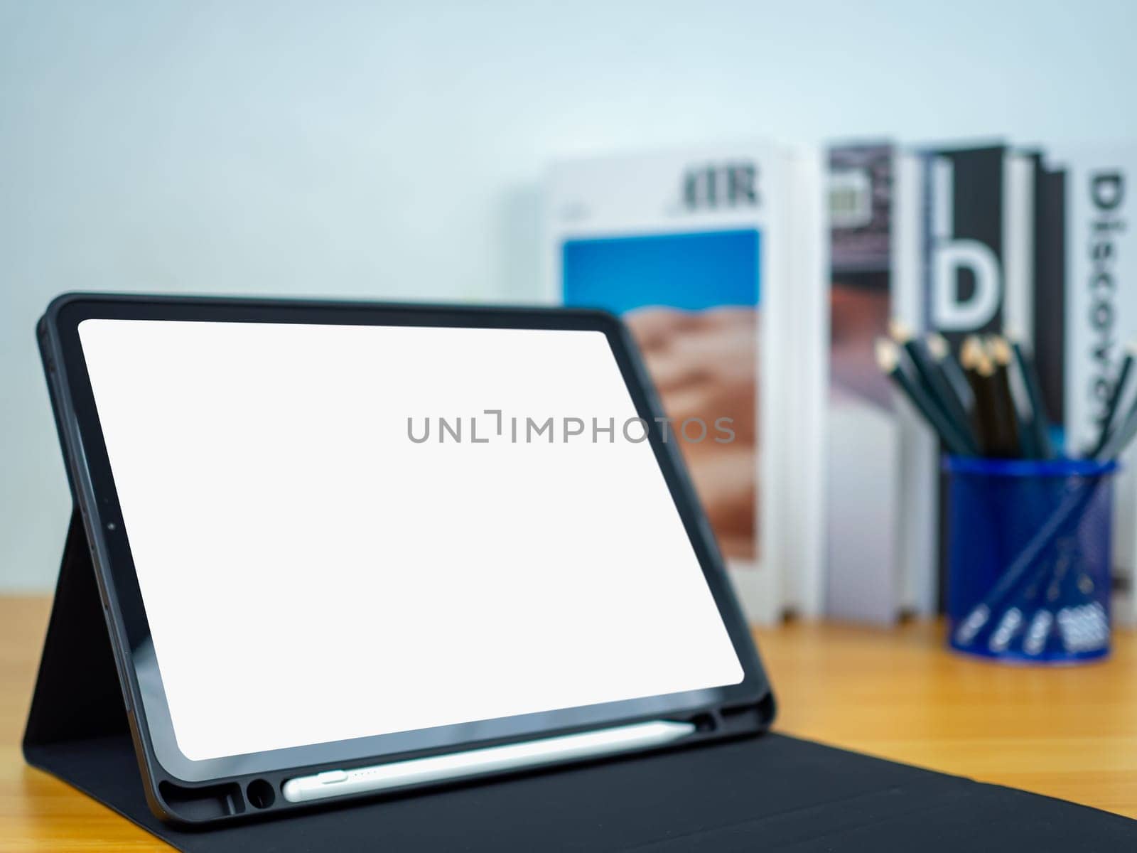 Tablet with blank screen on wooden table. Office supplies, Books on wooden table and white wall. Space for copying your text, Workspace and copy space, Desk with office supplies.
