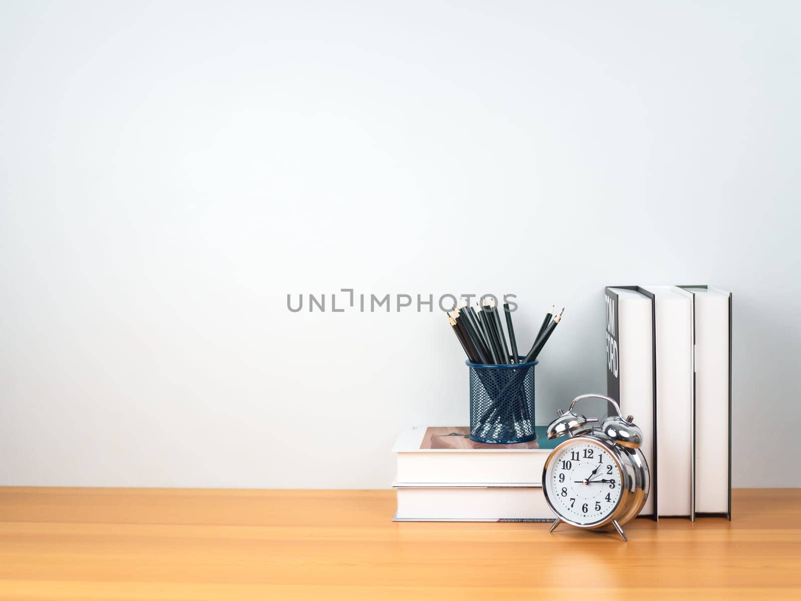 Back to school concept, Pencil on book stack and alarm clock on wooden table workspace area and white wall, Concept of time to study, read books, Concept of preparing for exams.