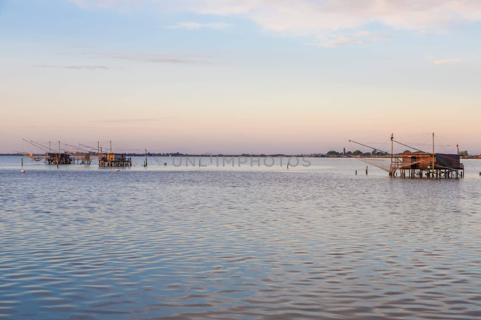 Italy, Comacchio lagoon. Panorama with traditional house for fishing at sunset