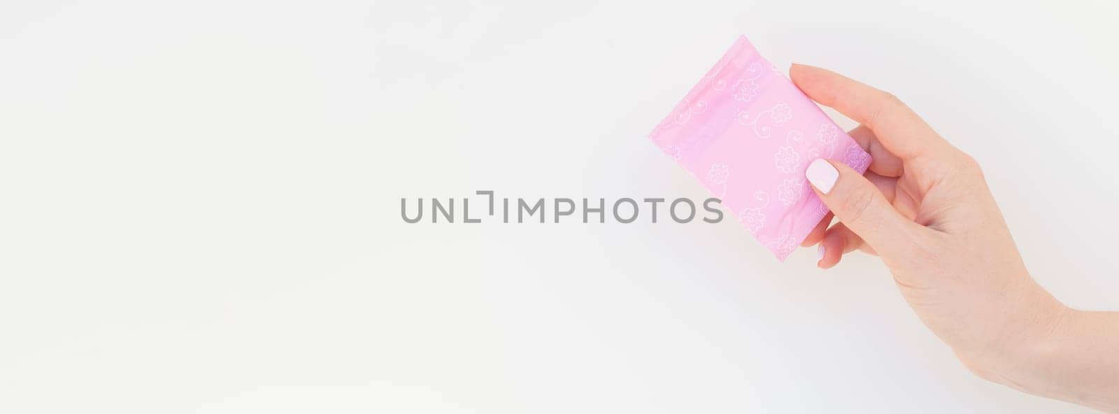 Woman hand with pastel manicure polish holding pink daily sanitary napkin isolated on white background with copy space. Long wide banner for feminine beauty blog social media Female healthcare concept