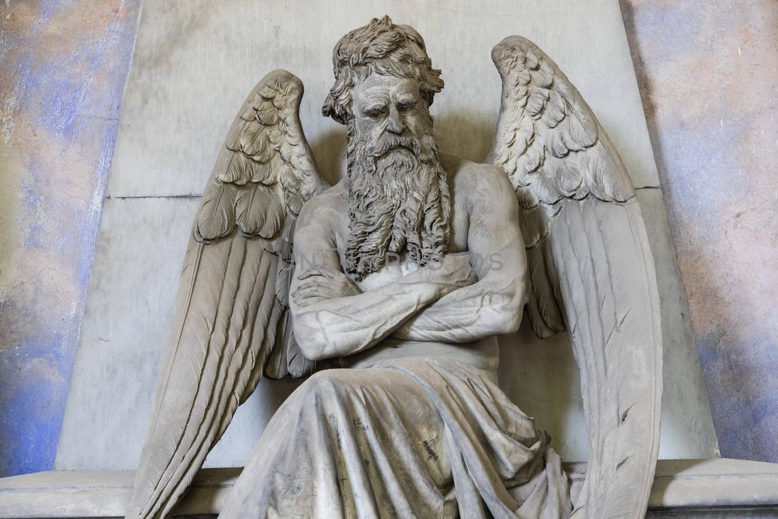 Old angel statue sitting on a tomb in contemplation. Memory and nostalgia