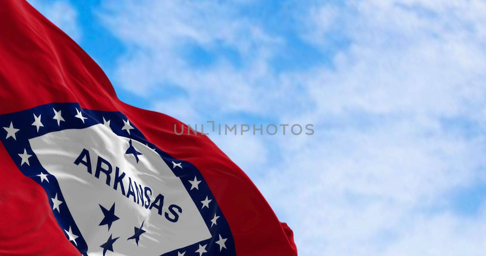 Arkansas state flag waving in the wind on a clear day. Red field with blue-bordered white diamond. 29 stars and ARKANSAS in blue. 3d illustration render. Selective focus. Fluttering fabric.