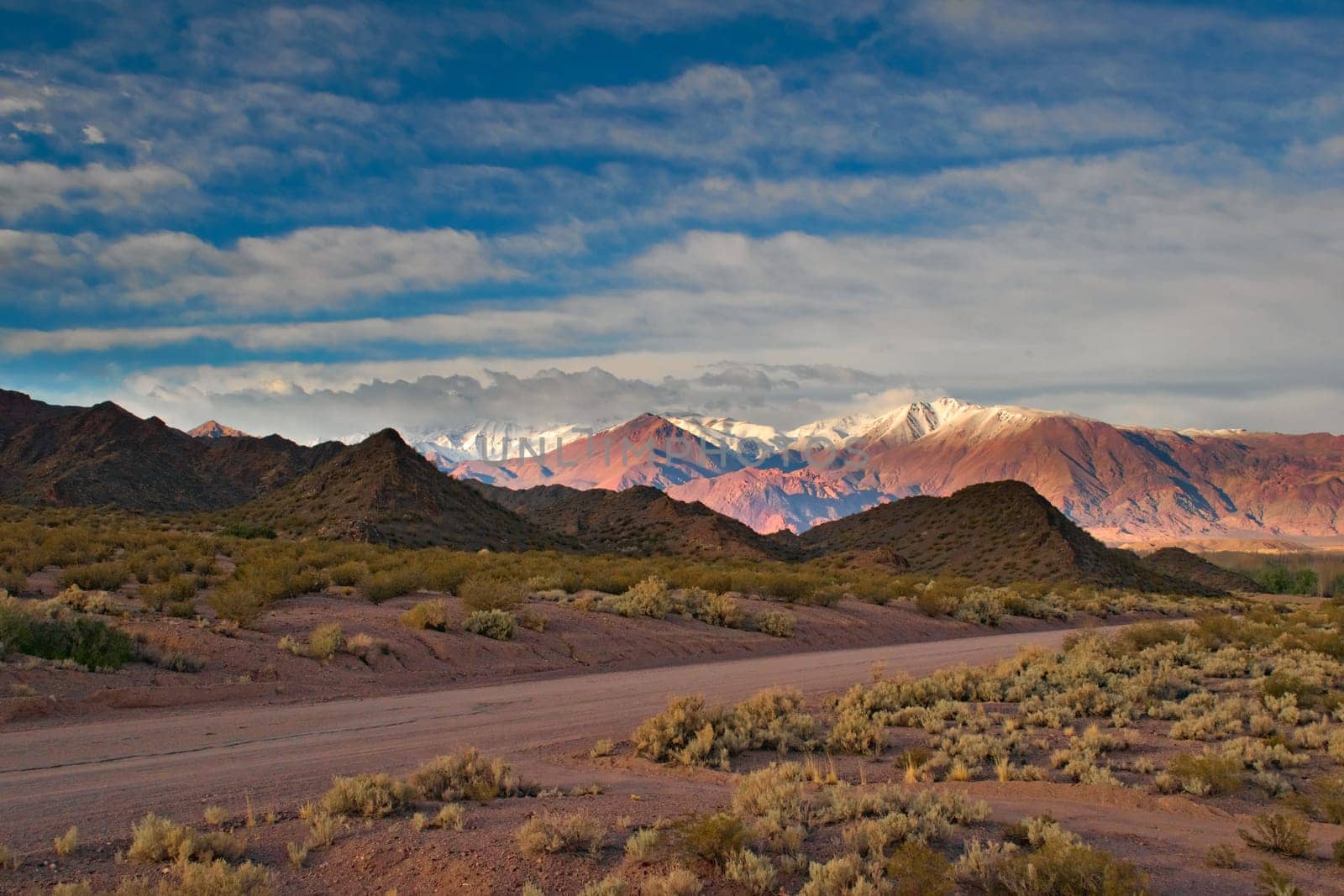 Dirt road and snow capped Andes mountains at dawn near Uspallata, Argentina.