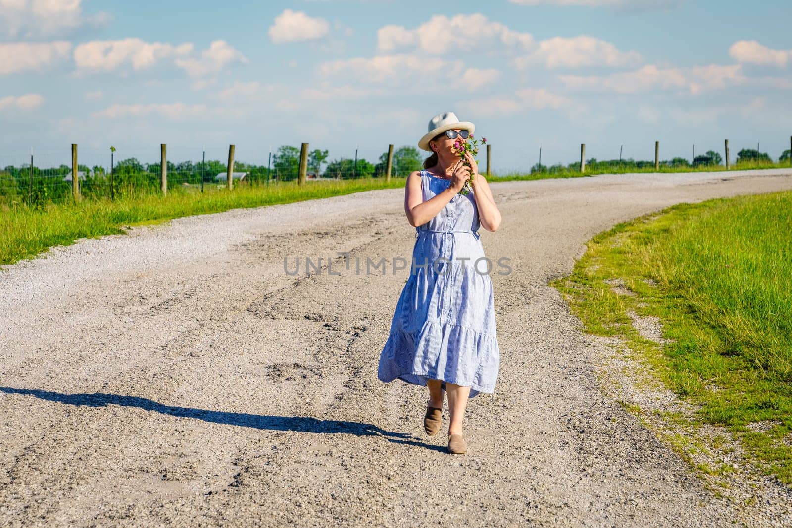 Happy mature woman is walking along a rural road on a bright summer day.
