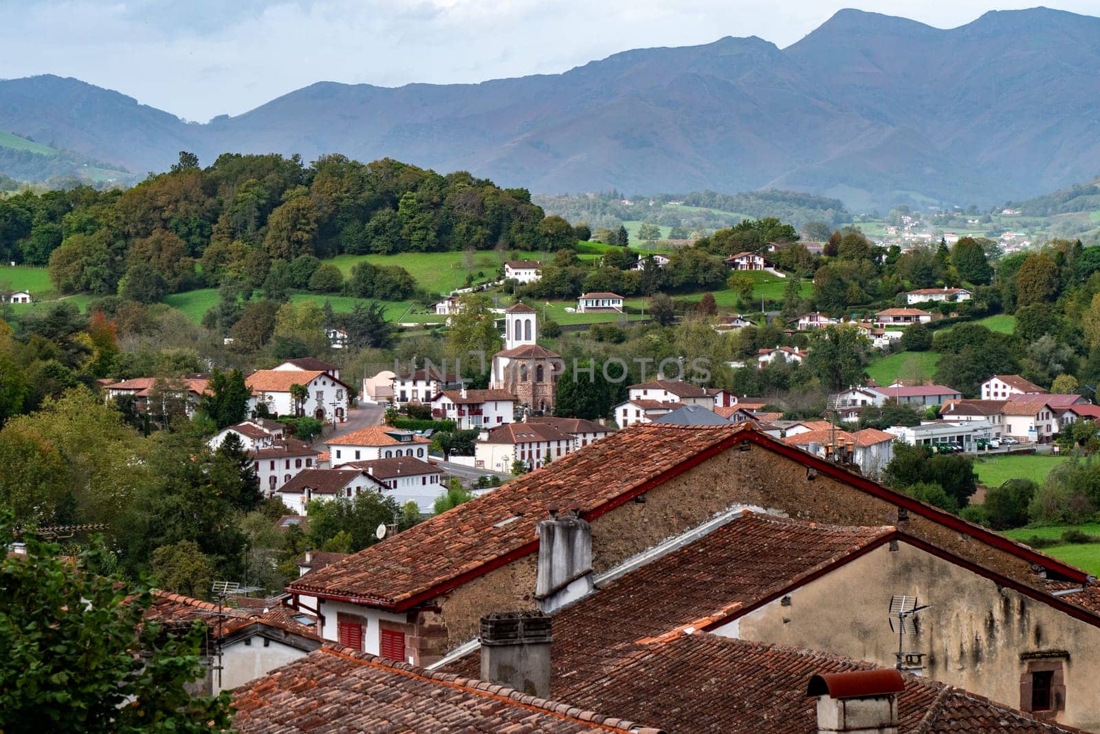 Saint Jean Pied de Port, houses and a church. The houses are mostly white and the church is brown. The town is surrounded by mountains