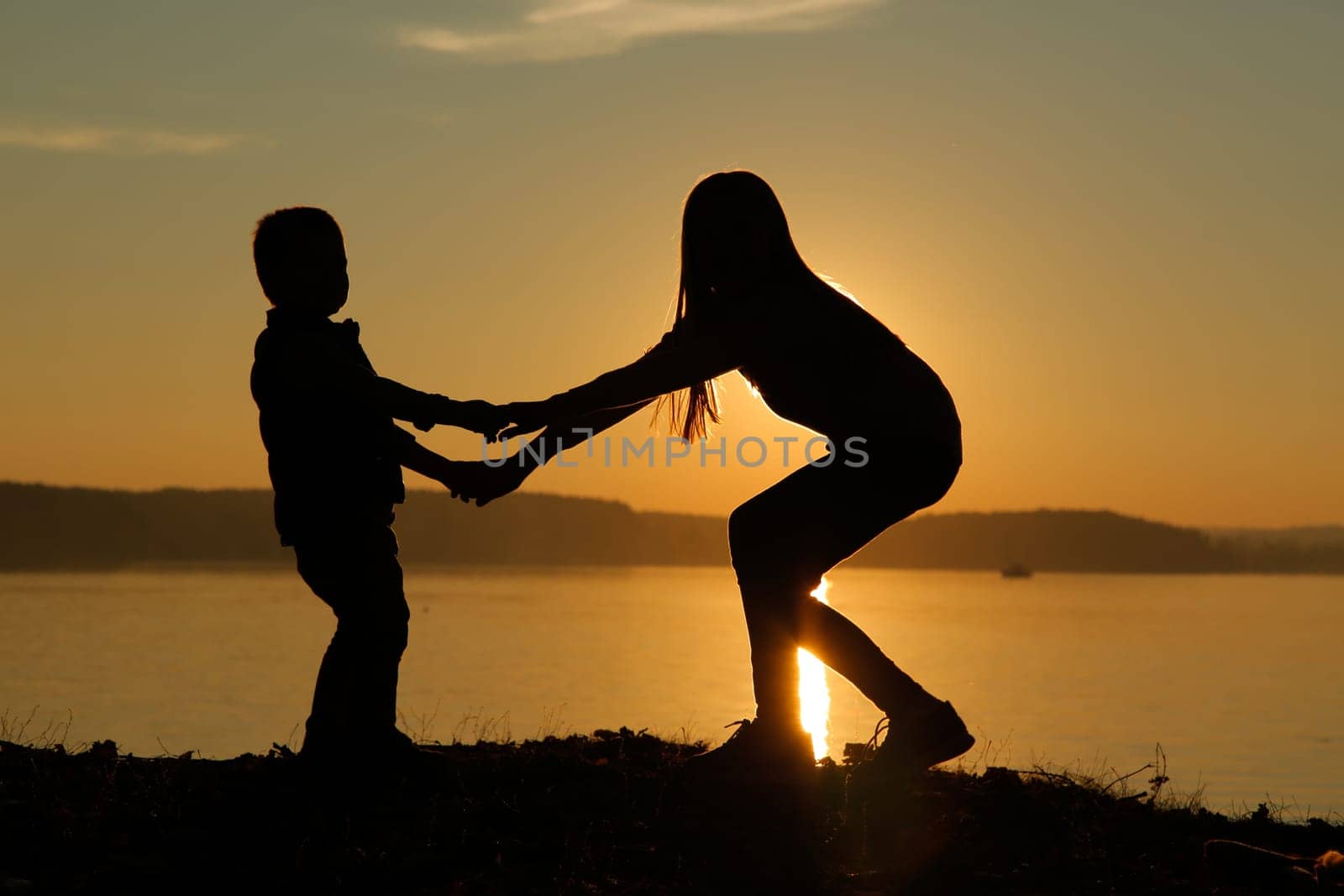 A stunning and beautiful silhouette at sunset depicting children happily cuddling up to each other at the water's edge