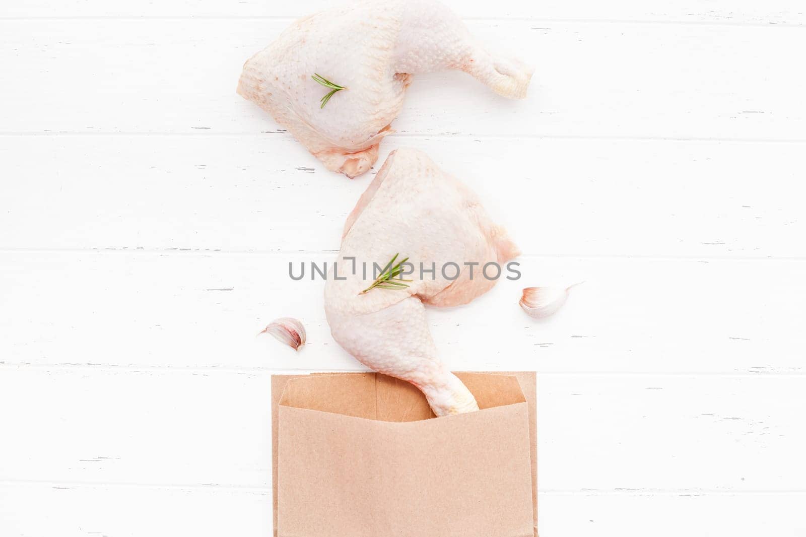 Creative Top view flat lay of fresh raw chicken legs with rosemary herbs garlic tomatoes on white wooden background with copy space. Food preparation recipe cooking concept
