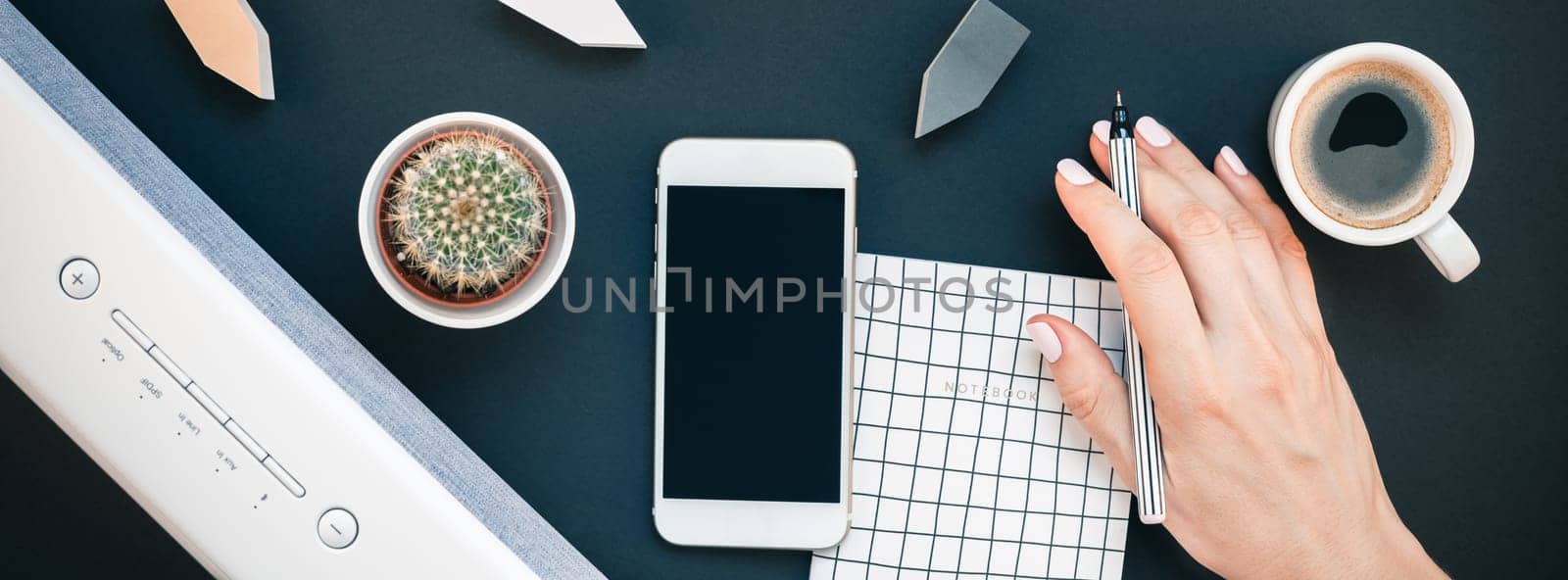 Top view flat lay of feminine desk workspace with white stereo bluetooth soundbar and smartphone for music listening and coffee cup with copy space on black background. Template for blog social media