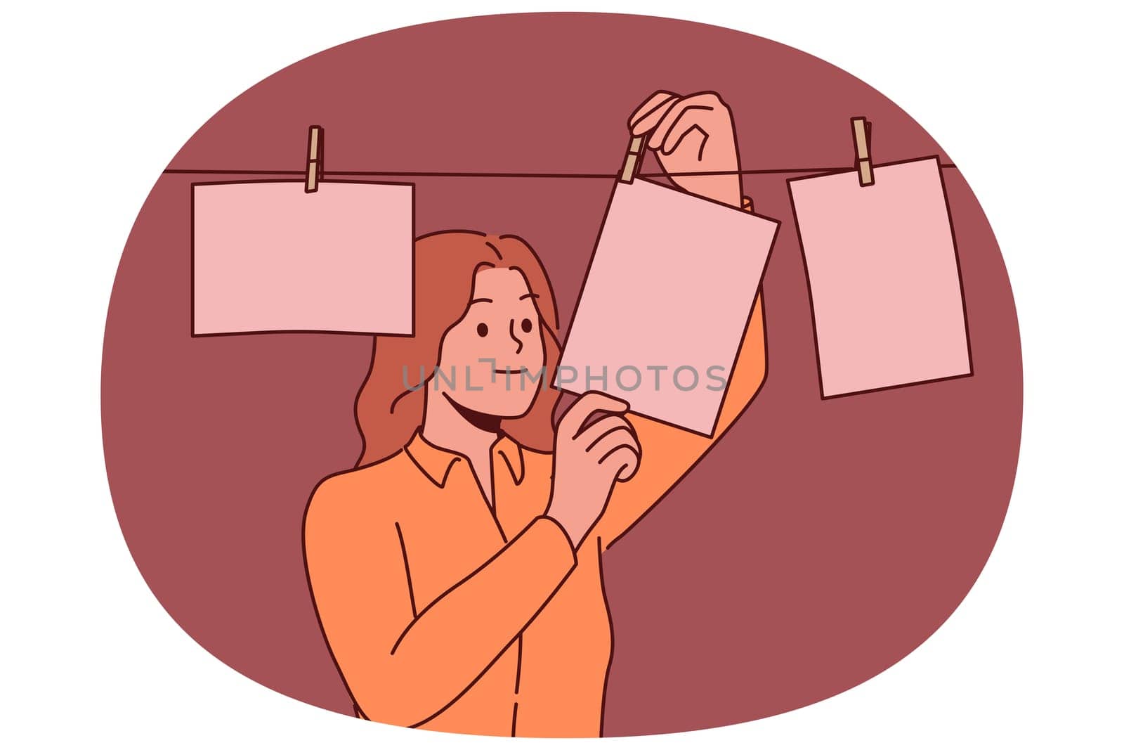 Woman photographer stands in room for developing photographs using old technology and looks at pictures hanging on rope. Girl photographer is fond of creating photos with use of equipment last century